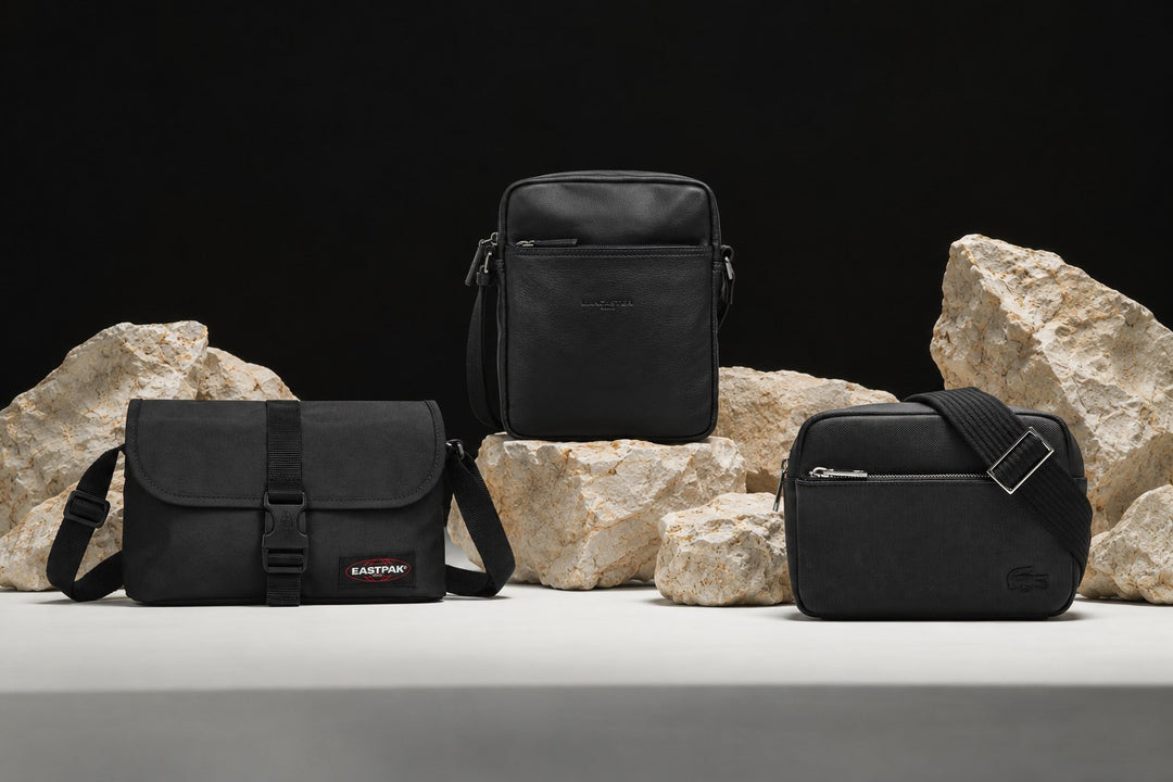 Sacoches homme Eastpak, Lancaster et Lacoste noires posées parmi des pierres claires