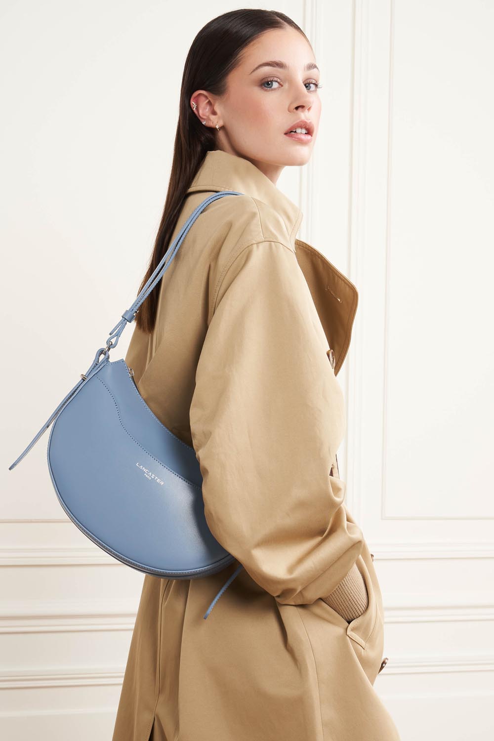 Lancaster, besace Suave Ace bleue portée en bandoulière avec un trench beige.