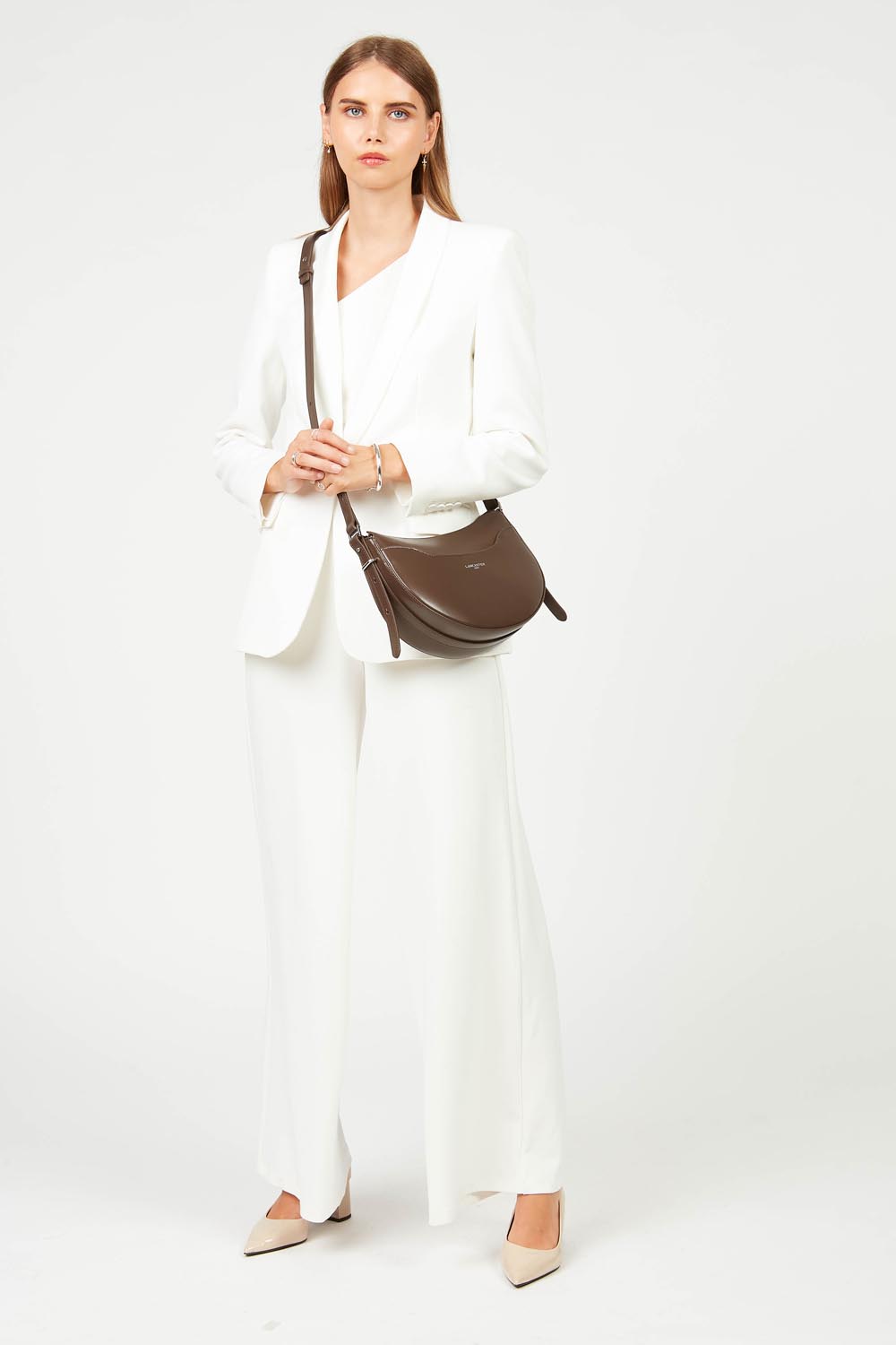 Lancaster besace Suave Ace marron portée en bandoulière sur une tenue blanche.