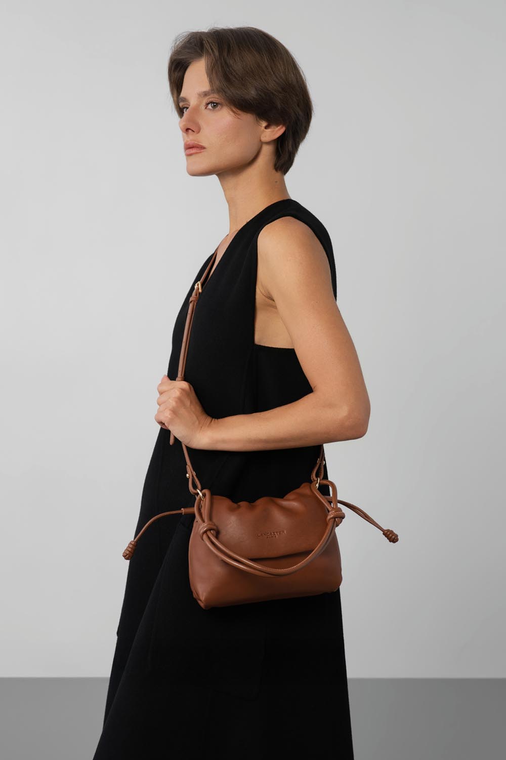Lancaster, besace Lush marron portée à l’épaule sur une robe noire.