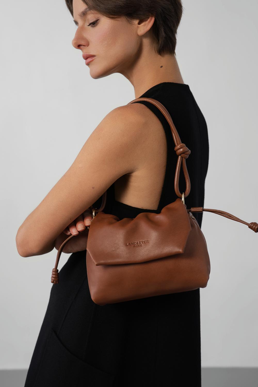 Lancaster besace Lush marron portée à l’épaule, avec une tenue noire.