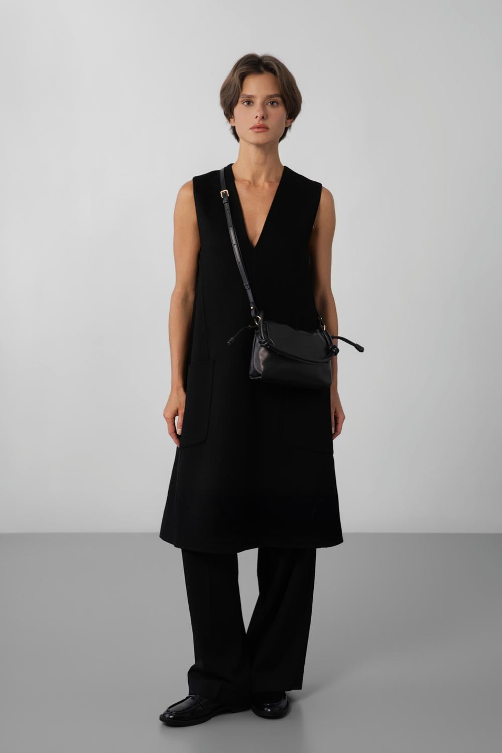 Lancaster besace Lush noire portée en bandoulière sur une robe sans manches et un pantalon noirs.